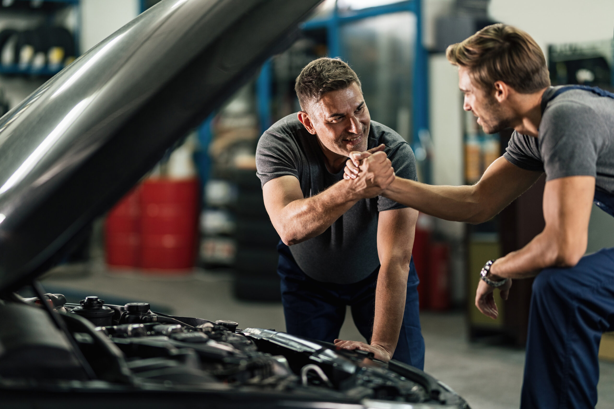 Two auto mechanics giving each other a manly greet in in auto repair shop.